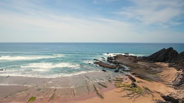 Dramatic aerial view of the atlantic ocean waves washing over the unique rock formations and sandy beaches of costa vicentina near aljezur in algarve, portugal, on a bright sunny day