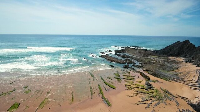 Dramatic aerial view of the atlantic ocean waves crashing on the unique rocky shores and sandy beach of aljezur in costa vicentina, portugal, revealing stunning geological formations