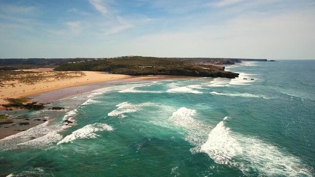 Aerial footage capturing the beautiful turquoise waves of the atlantic ocean breaking along the sandy shore of amoreira beach on the stunning vicentina coast in aljezur, algarve, portugal