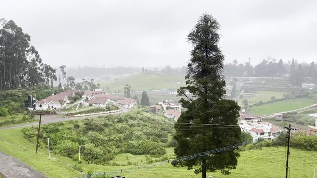 4K panning view of misty hill station cottages with red tiled roofs among lush tea gardens, eucalyptus trees and foggy slopes, capturing peaceful monsoon travel and countryside retreat.