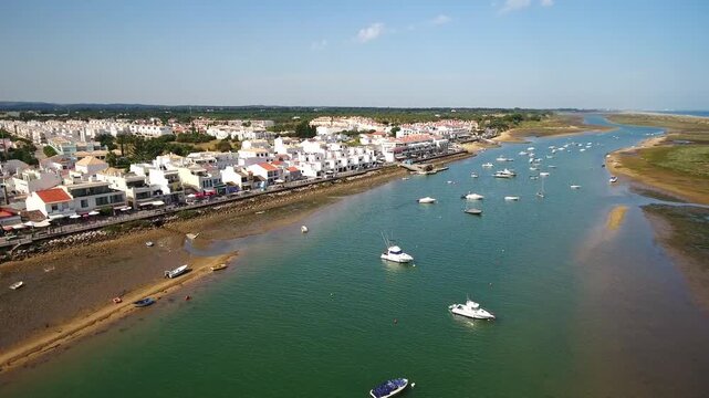 Beautiful aerial footage showing the picturesque village of cabanas de tavira with its white houses and the tranquil waters of ria formosa natural park, dotted with moored leisure boats