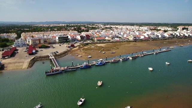 Beautiful aerial footage showing the picturesque fishing village of cabanas de tavira in the sunny algarve region of portugal, featuring its charming harbor and boats on the ria formosa lagoon