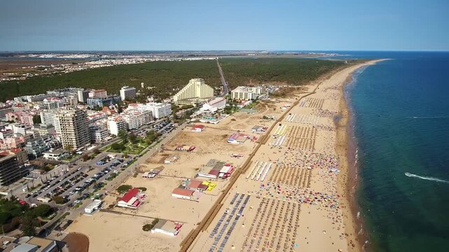 Majestic aerial view of the crowded beach of monte gordo, a popular tourist destination in algarve, portugal, with colorful umbrellas dotting the golden sand next to the city