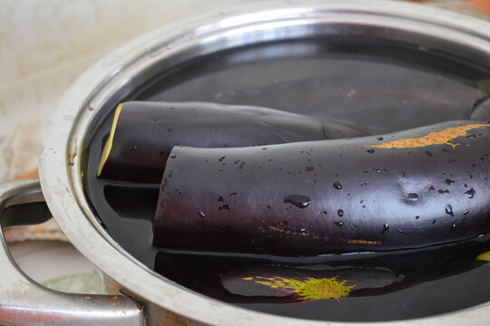 Whole purple eggplants soaking in a pot of water close-up. Vegetable soaking to remove bitterness, food preparation, raw ingredients and domestic cooking process concept.