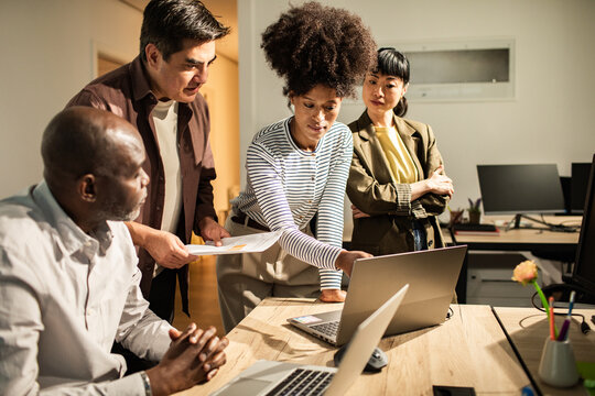 Diverse coworkers collaborating on laptop in modern office