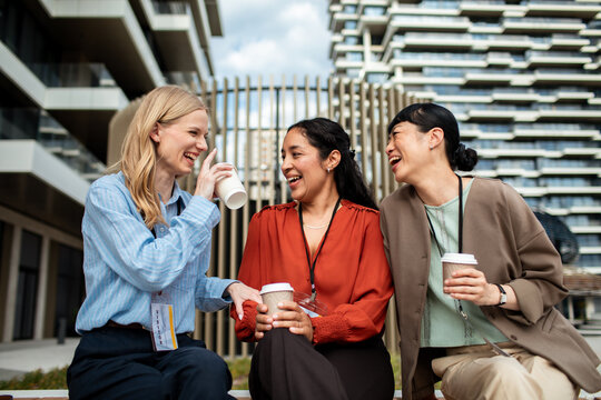 Three coworkers laughing over coffee outside a modern office building