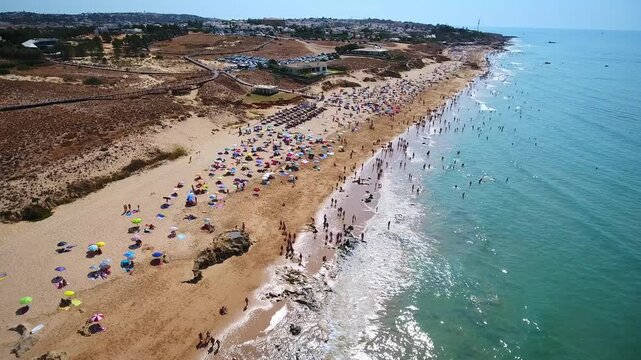 High aerial view of tourists relaxing and swimming at praia da gale, a popular sunny destination in albufeira, portugal, with colorful umbrellas on the golden sand and blue ocean waves