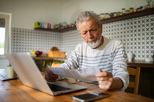 Senior man reviewing bills at home kitchen table