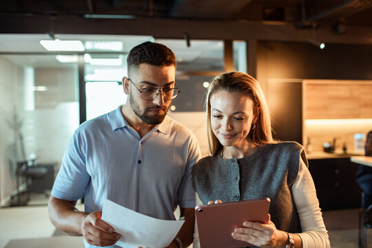 Two coworkers reviewing document and tablet in modern office