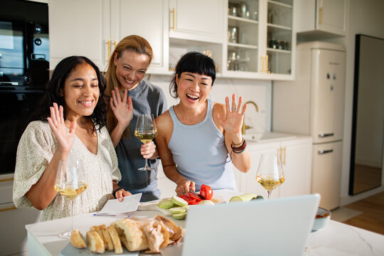Three friends waving during online cooking class in modern kitchen