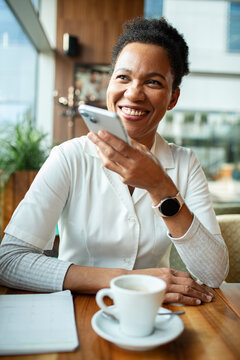 Smiling woman using voice assistant on smartphone at cafe