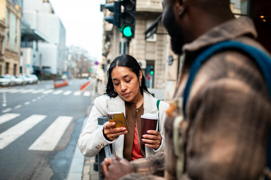 Woman using smartphone with coffee at city crosswalk