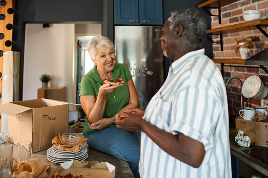 Senior couple sharing pizza while unpacking in kitchen