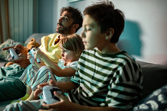 Father and children playing video games on the couch at home