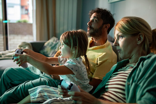 Parents and child playing video games on living room sofa