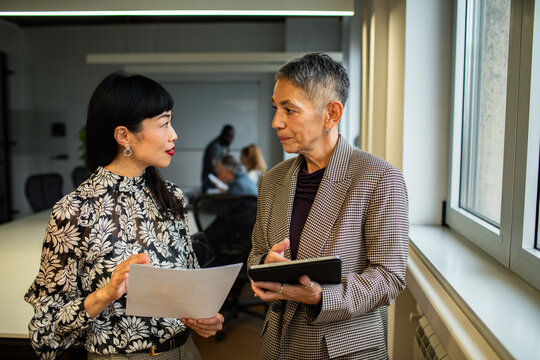 Two professional women discussing project by window in office