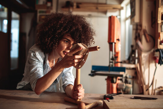 Young woman sanding wooden stool in workshop