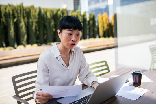Professional woman reviewing documents on laptop at outdoor cafe