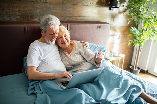 Smiling senior couple online shopping in bed at home