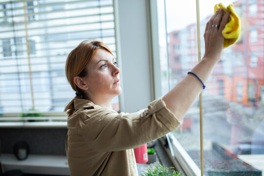 Young woman cleaning apartment window with cloth