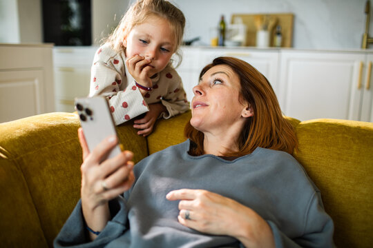 Mother and daughter using smartphone on couch at home