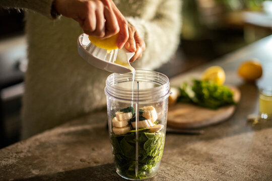 Hands squeezing lemon into blender cup for green smoothie in home kitchen