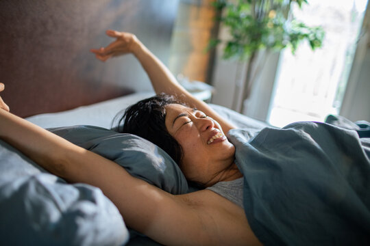 Smiling woman stretching in bed at home