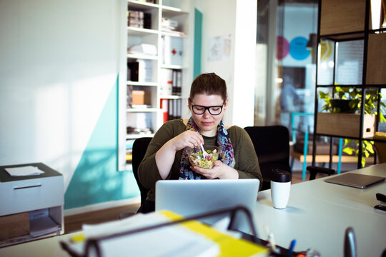 Woman eating salad at desk in modern office