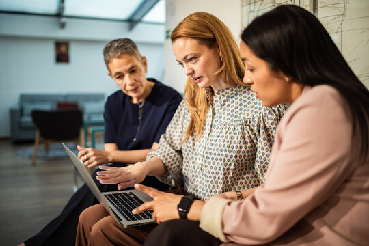 Three businesswomen collaborating on a laptop in office lounge