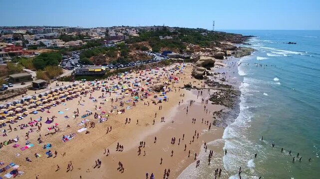 Stunning aerial view showing crowds of people relaxing and sunbathing on the sandy shore of gale beach in algarve, portugal, with tourists enjoying the beautiful turquoise ocean waters