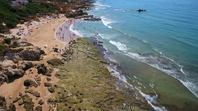 Aerial view of the beautiful gale beach coastline in albufeira, algarve, with tourists swimming in the turquoise ocean water and relaxing on the golden sand during a sunny summer day