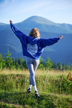 Woman tourist on grassy hill with beautiful mountain landscape with Hoverla in background. Young female wearing blue hoodie and grey leggings.