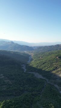 High angle aerial drone view of green mountain valley and dry river bed flowing toward Thessalian plain in Pindus range Greece vertical stock video. High quality 4k footage