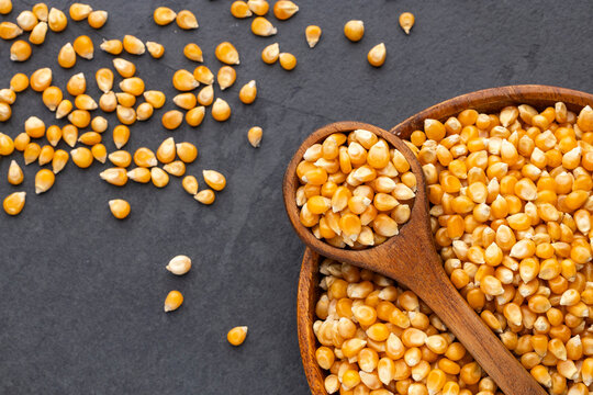Popcorn kernels presented in wooden utensils on a dark surface, ideal for food and cooking concepts