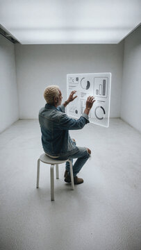 Man with white hair interacts with glowing translucent digital data screen containing bar charts and circular graphs in a bright minimalist studio setting.