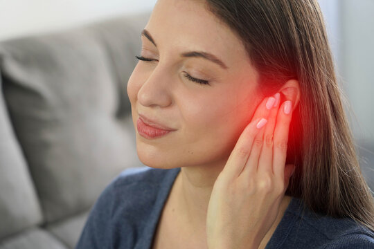 Young woman covering her ear with hand and tilting head in pain from otitis or earache