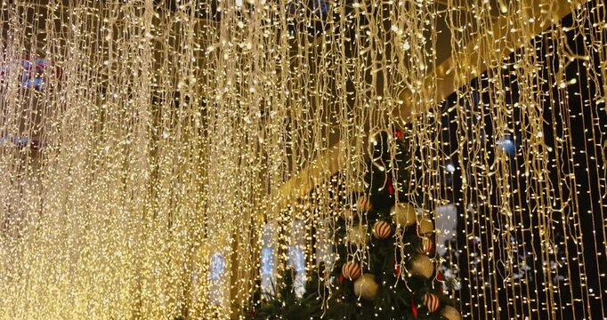 Christmas fairy lights hanging from ceiling in festive holiday display, warm LED curtain illuminating decorated tree, commercial seasonal background.