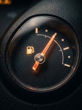 Fuel gauge with glowing orange needle on car dashboard, automotive gas level indicator, vehicle fuel tank meter showing low energy