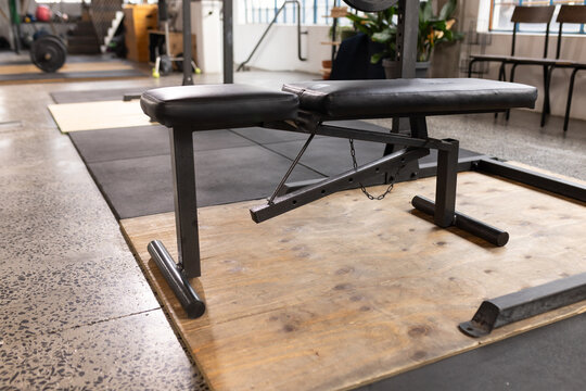 Adjustable padded weight bench is resting on wooden platform in gym, with barbell nearby