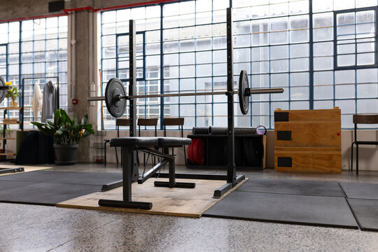 Bench press station is occupying center in loft gym on wooden lifting platform with loaded barbell