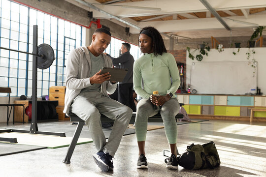African American workout pair talking through workout on tablet while holding sports drink on bench