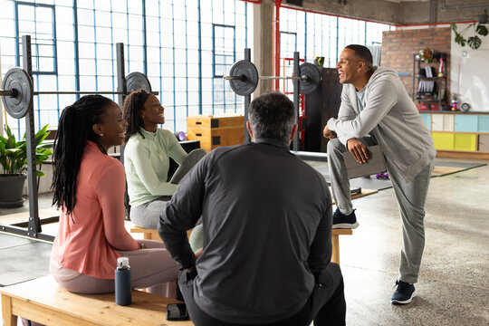 Diverse fitness group listening while trainer standing right in studio holding tablet, copy space
