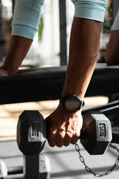 African American male gripping 8kg dumbbell on gym bench, wearing blue top and black smartwatch