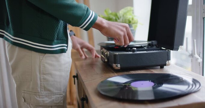 Listener's hands are lowering tonearm to play music, then are swapping vinyl on console near window