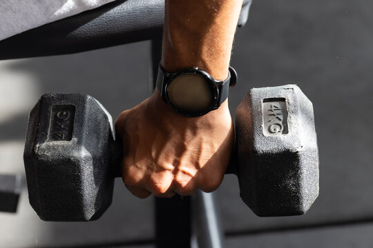 African American man gripping 4 KG hex dumbbell while wearing smartwatch at gym bench