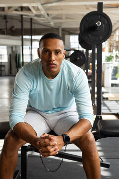 African American adult male sitting on flat weight bench resting between sets with loaded barbell