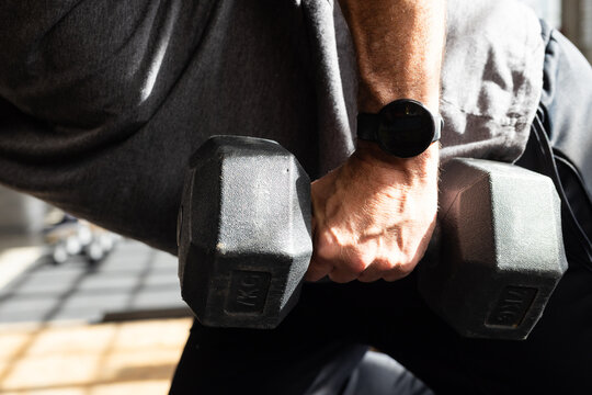 Forearm is gripping hex rubber dumbbell and bracing on padded bench, casting window-grid shadows