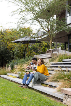 African American couple sipping ceramic mugs, sitting on tiered concrete steps in backyard garden