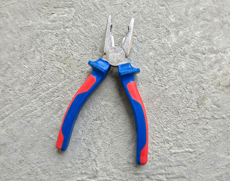Professional steel pliers with blue and red rubberized handles on concrete background.