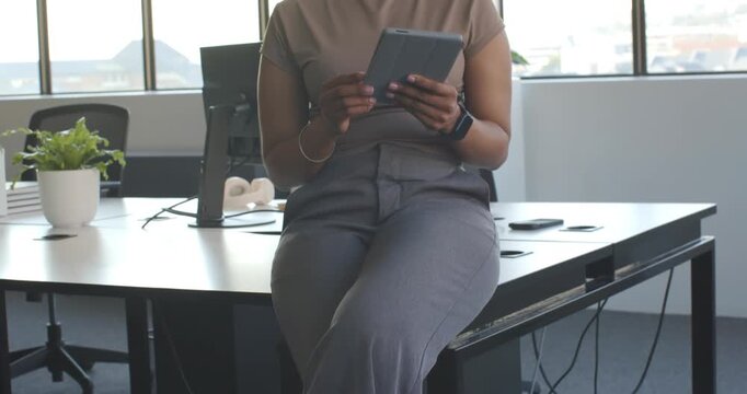 Camera rising revealing adult African woman at desk, tapping tablet, reading emails before meeting